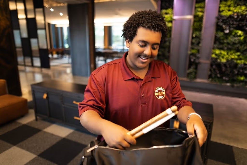 Young Black male in red shirt placing drum sticks in his bookbag
